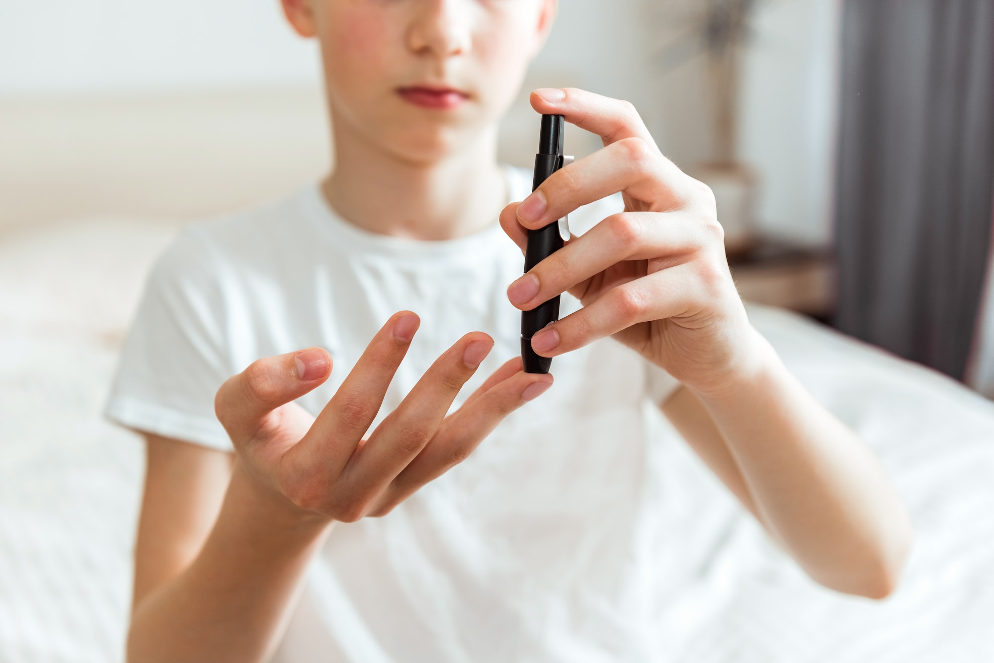 Teen boy takes a blood sample for diabetes with lancet pen. Problems of diabetes